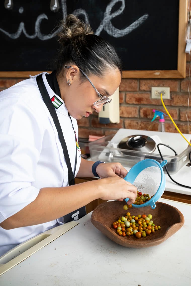 A contestant strains small wild tomatoes in her prep area.