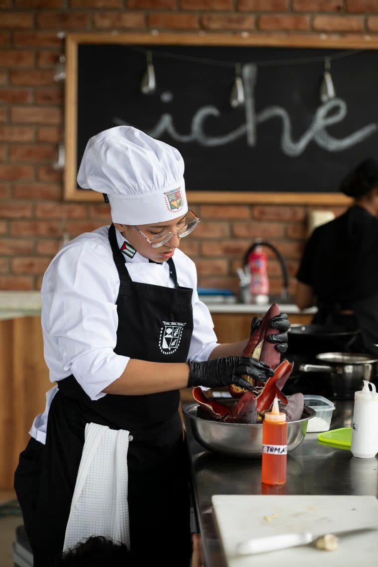 A contestant cleans a reddish ingredient wearing black gloves.