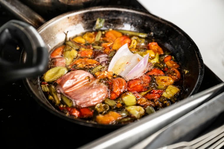 Chili peppers, tomatoes and vegetables browning in a pan.