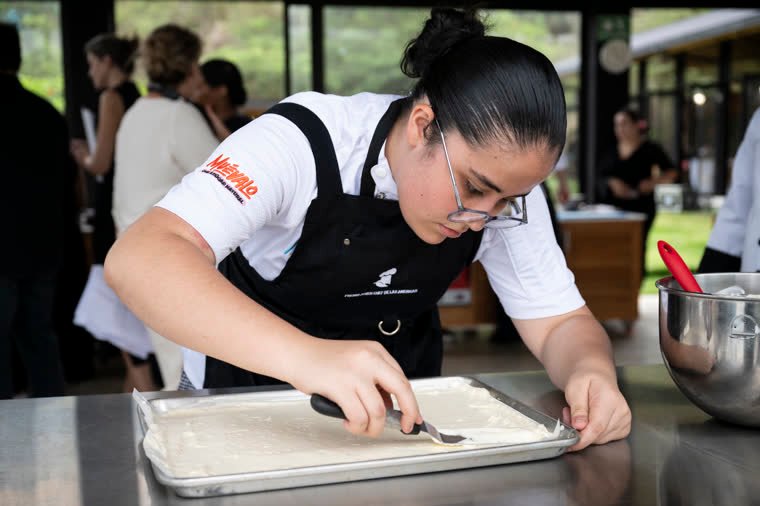 A contestant carefully spreads a light mixture over a tray.