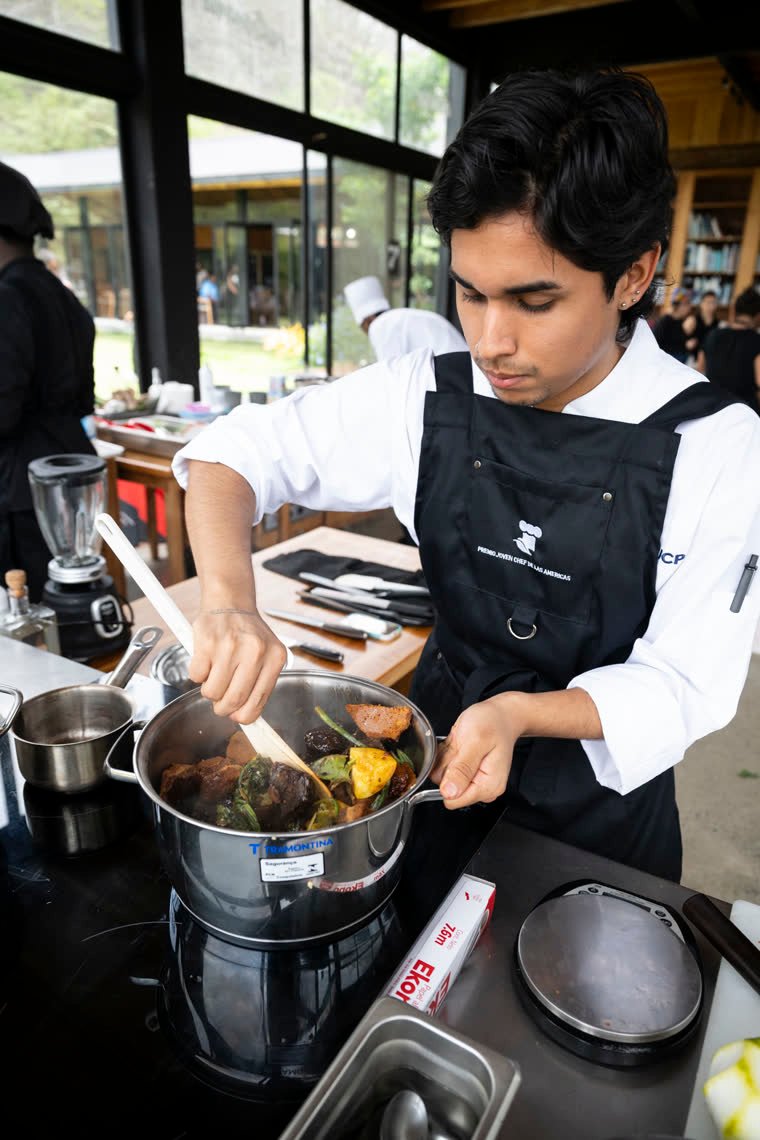 A contestant stirs a preparation in a pot at the cooking station.