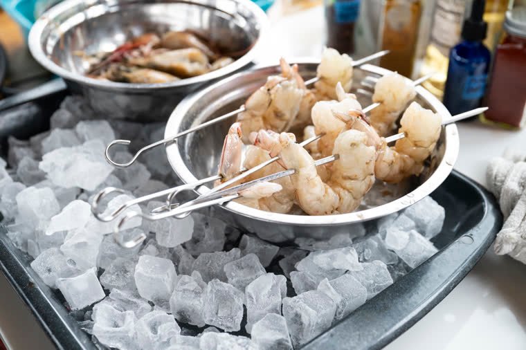 Shrimp skewers on ice in a metal container, ready to cook.