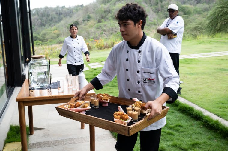 A contestant carries a tray of portions of the dish toward the presentation area.
