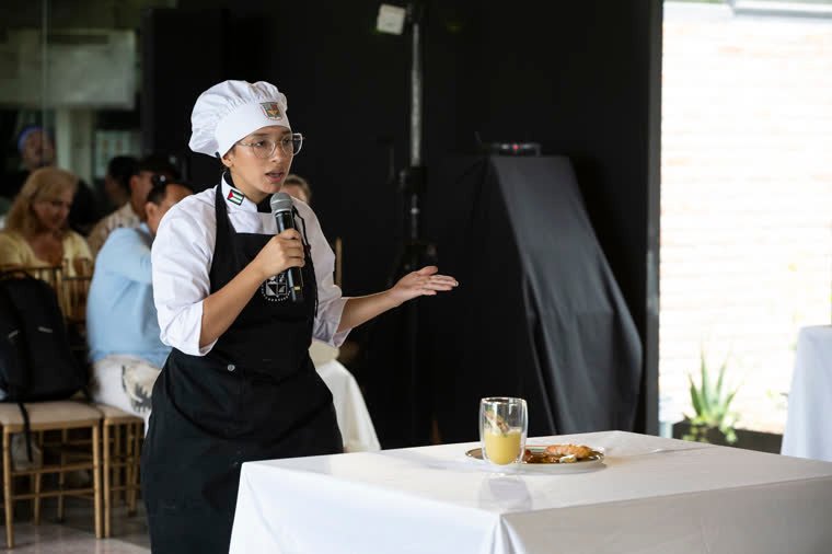 A contestant explains her dish to the attendees, microphone in hand.