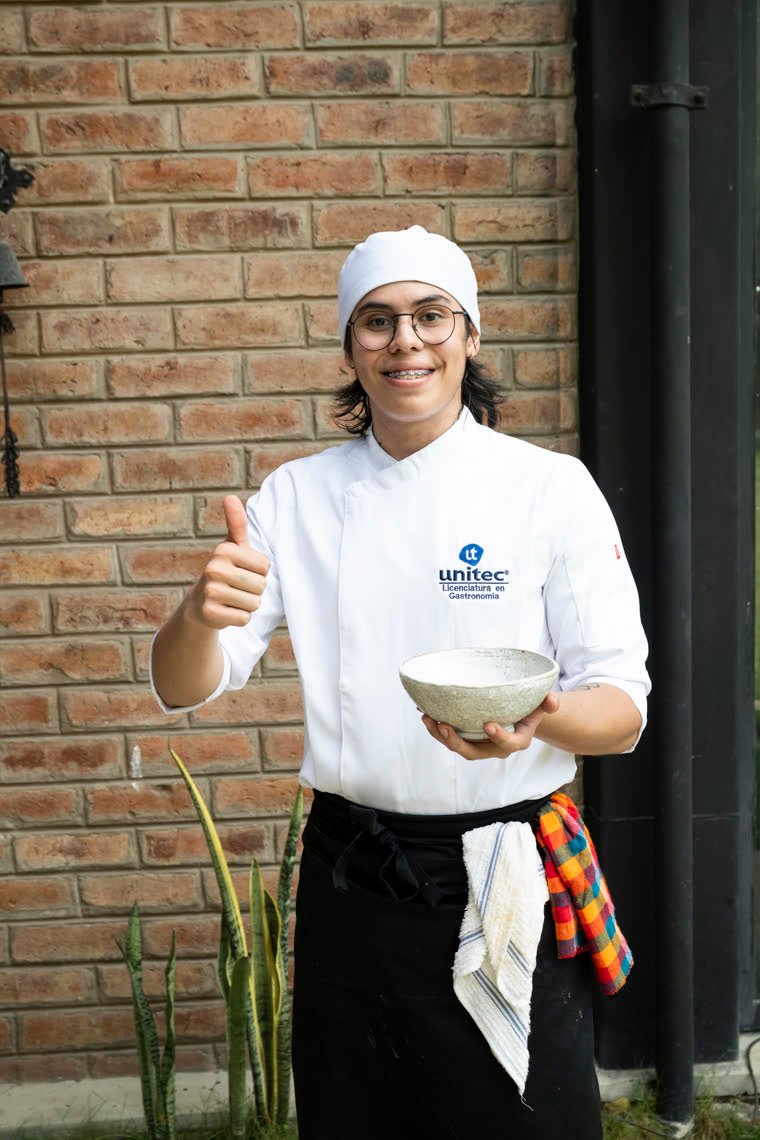 A contestant smiles with a thumbs up, holding his bowl in front of a brick wall.