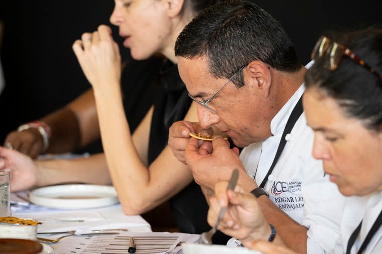 A judge smells and tastes a bite while the others evaluate.