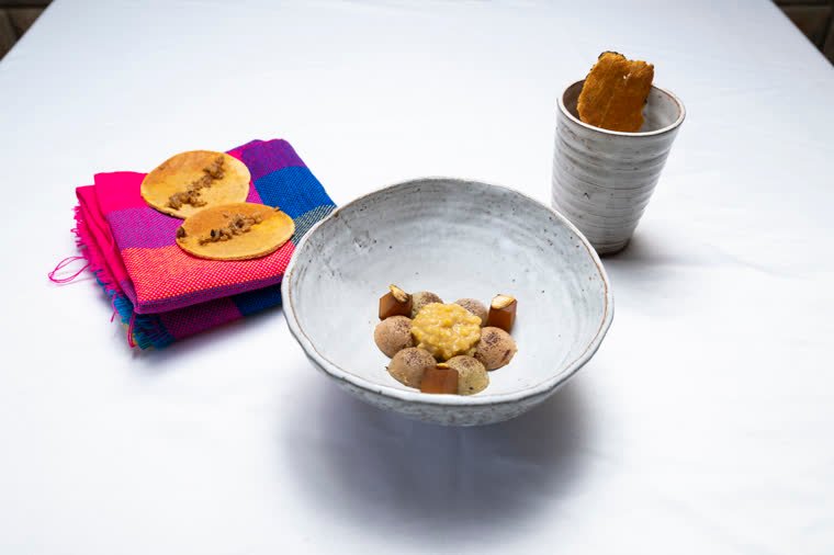 Dish in a ceramic bowl with golden elements, served with tortillas on a colorful textile and a glass.