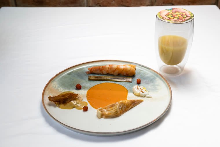 Dish with shrimp, orange sauce and garnish, served with a drink in a double-wall glass.