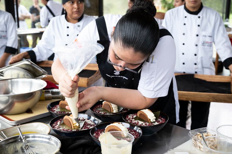 A contestant decorates several plates with a piping bag at the kitchen station.