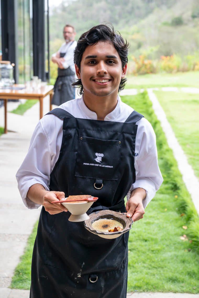 Portrait of a smiling young chef with two preparations in his hands.