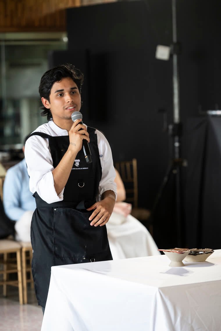 A contestant explains his dish at the microphone before the audience.