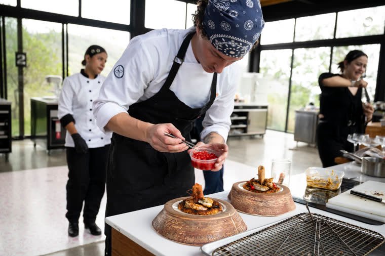 A contestant in a blue bandana places the final detail with tweezers on his plate.