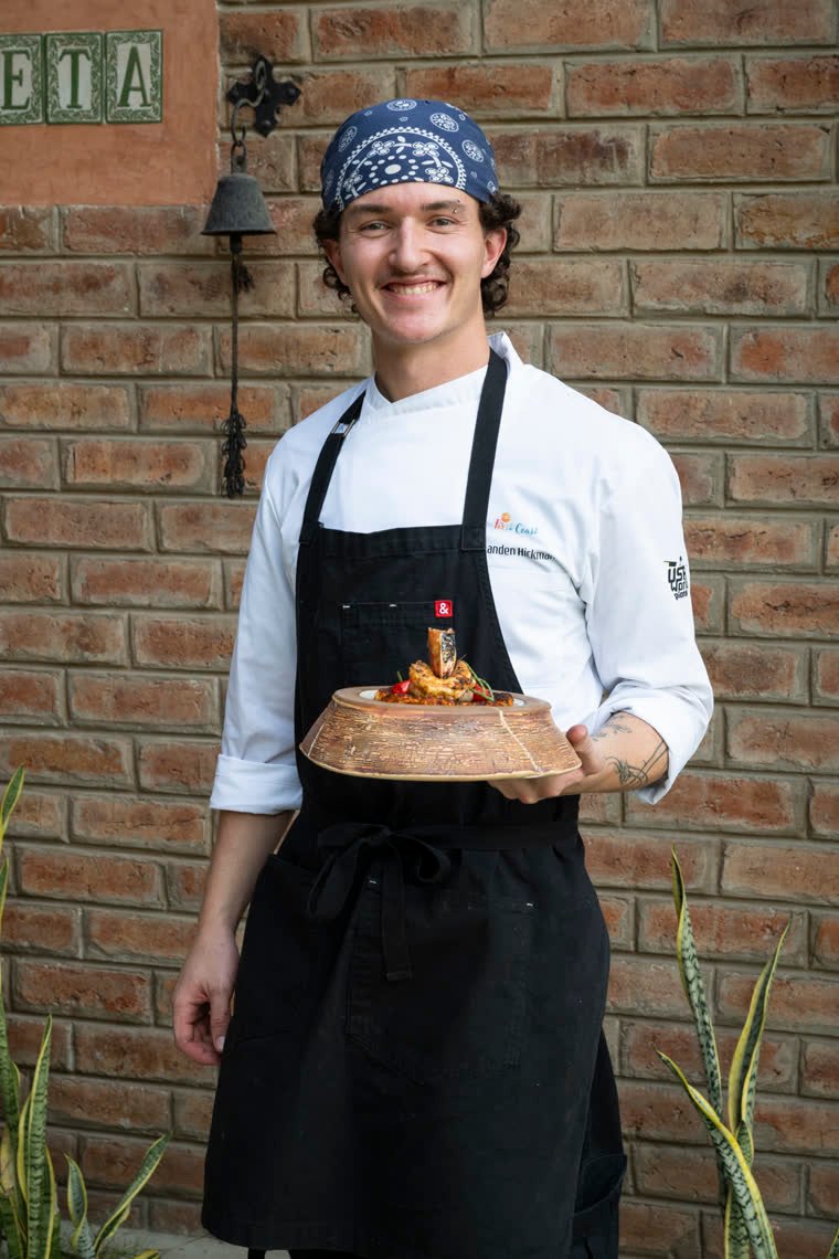Portrait of a contestant in a blue bandana holding his finished dish.