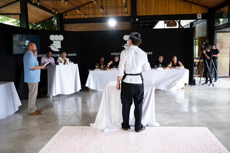 A contestant presents his dish standing before the jury table in the competition hall.