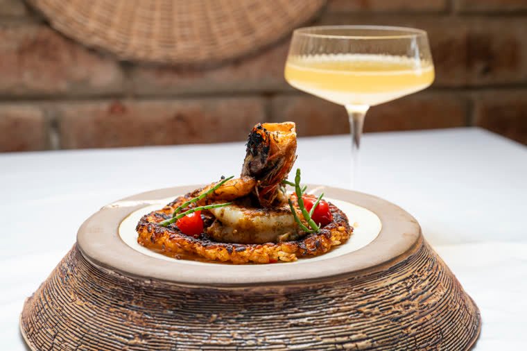 Finished shellfish dish on a golden, crispy base, with a citrus cocktail in the background.