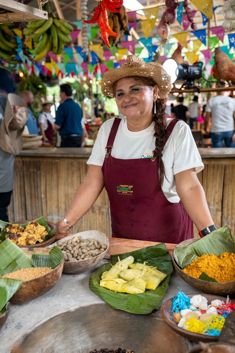 Portrait of a cook in a maroon apron behind a table of traditional preparations.