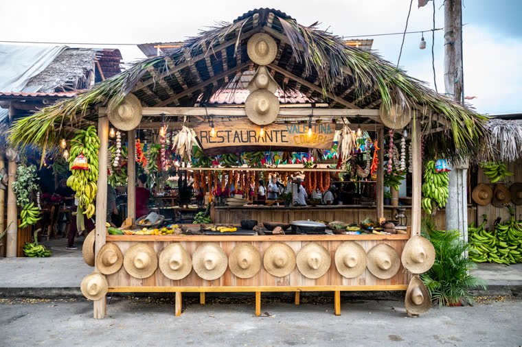 Front of a thatched-roof restaurant, with hats and an open kitchen.
