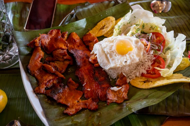 Dish served on a banana leaf with marinated meat, rice, fried egg and fried plantain.