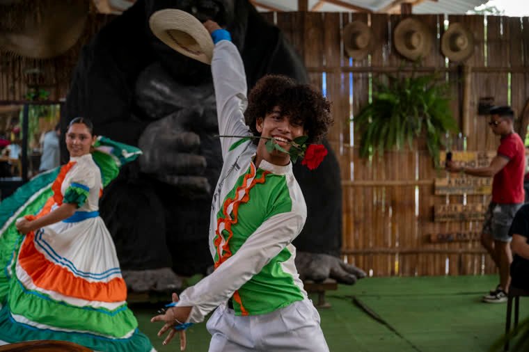 Dancers in colorful traditional costumes, one with a rose between his teeth.