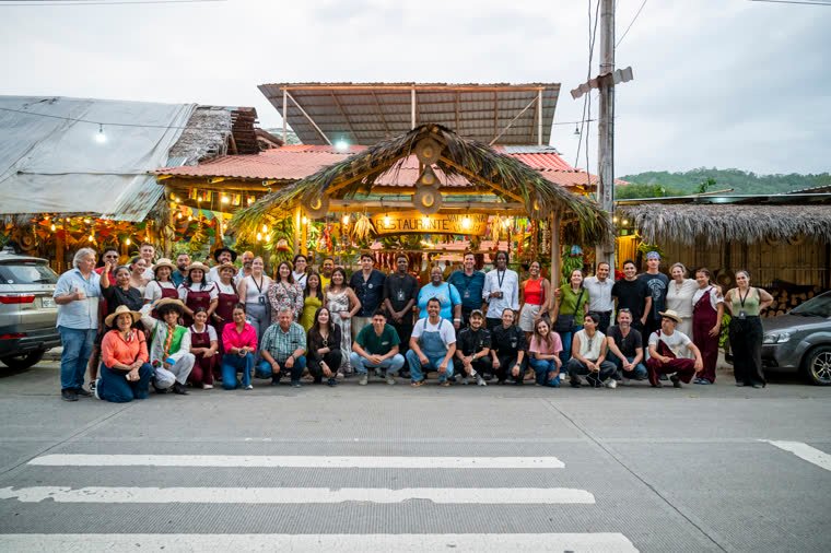 Large group photo in the street, in front of the restaurant’s lit entrance.